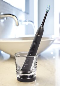Elektrische Zahnbürste mit schwarzem Griff, fünf Reinigungsmodi und blau-grünen Borsten, aufrecht in einem klaren Glashalter platziert.