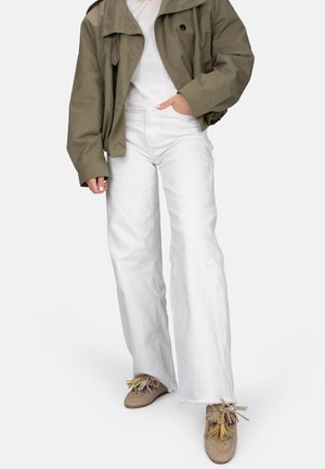 Weiße breite Jeans, olivgrüne übergroße Jacke und beiges Schuhwerk mit bunten Quasten. Einfaches Design mit lässiger Passform und Textur.