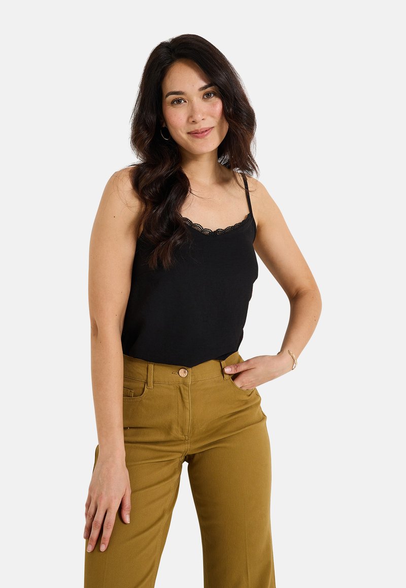 Camisón negro con encaje, combinado con pantalones mostaza de cintura alta con bolsillos y cierre frontal de botón, lucido por un modelo.