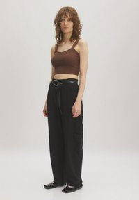 Brown ribbed crop top with wide straps paired with black wide-leg pants featuring a belted waist and side pockets. Black flat shoes.
