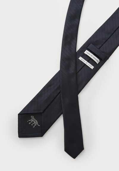 Tumši zila kaklasaite ar teksturētu diagonālu rakstu, kuras galā ir balts tīģera logo. Uz etiķetēm norādīts "Tiger of Sweden" un "Made in Italy."