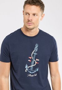 T-shirt en coton bleu marine avec un graphique d'ancre, une chaîne et des accents rouges, col rond, manches courtes et coupe décontractée.