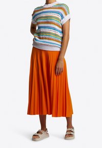 Neulottu lyhythihainen paita monivärisillä raidoilla, yhdistetty laskostettuun oranssiin midihameeseen ja valkoisiin sandaaleihin, joissa on säädettävät hihnat.
