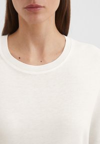 Ljust beige tröja med rund halsringning, tillverkad av mjukt tyg. Texturen ser jämn ut med subtila detaljer i fint stickat.