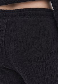 Černá texturovaná látka přiléhavých kalhot s zvrásněným designem. Obsahuje elastický pas a hladký povrch s jemnými variacemi.