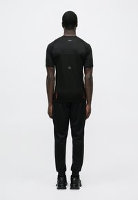 Melna sporta īsroku krekls ar gludu tekstūru, kombinēts ar melnām biksēm jogger stilā. Aprīkots ar smalkām sarkanām detaļām un logotipu aizmugurē.