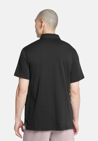Polo shirt nera a maniche corte, in materiale cotone, colletto classico, vista posteriore con orlo dritto e spacchi laterali per facilità di movimento.