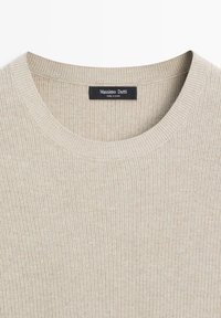 Pull en maille côtelée beige avec col rond et une étiquette de marque noire indiquant Massimo Dutti, fabriqué en Chine, cousue à l'intérieur du col arrière.