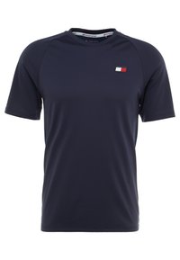 T-shirt de sport bleu marine à manches courtes avec un col rond et un petit logo rouge, blanc et bleu marine sur la poitrine gauche.