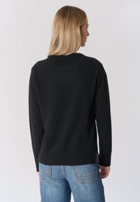 Maglione nero a maniche lunghe, scollo a girocollo e bordo a costine. Texture morbida, design semplice. Indossato con jeans in denim azzurro chiaro.