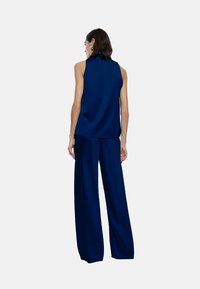 Top senza maniche di colore blu navy con collo alto e piega sul retro, abbinato a pantaloni a gamba larga dello stesso colore. Tessuto liscio, design minimalista.