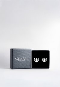 Silverhänge i hjärtform med intrikata utstansade mönster, visade i en smyckesask i svart sammet med en texturerad yta.