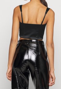 Musta satiininen crop-top, jossa on säädettävät hihnat ja sileä rakenne, yhdistettynä korkeavyötäröisiin mustiin kiiltävistä vinyylistä valmistettuihin housuihin, joissa on tyköistuva malli.