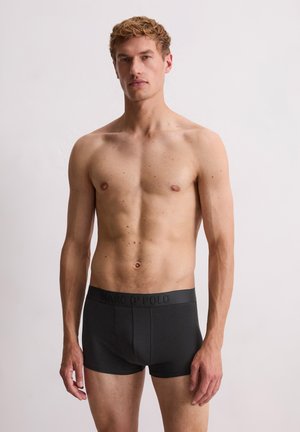 Boxer briefs noires en tissu doux, avec une ceinture confortable arborant un logo texturé. Le design est ajusté et minimaliste.