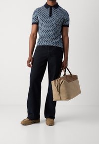 Granatowa koszulka polo z krótkim rękawem w wzory, ciemne dżinsy oraz jasnobrązowa skórzana torba z brązowymi akcentami. Casualowe obuwie z teksturowaną podeszwą.