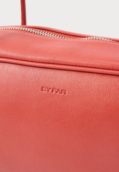 Kožená kabelka korálovo ružovej farby so strieborným zipsom a vystúpeným logom "BY FAR" na hladkom textúrovanom povrchu.