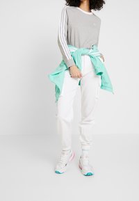 Grå långärmad topp med vita ränder, vita cargobyxor och färgglada sneakers. Ljusblå jacka knuten runt midjan.