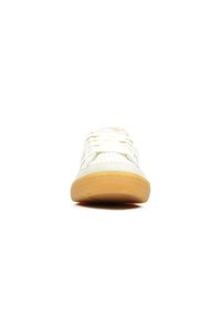 Witte sneaker met geperforeerde details, beige suede accenten, witte veters en een zool van rubber met een gumafwerking, gezien van voren op een witte achtergrond.