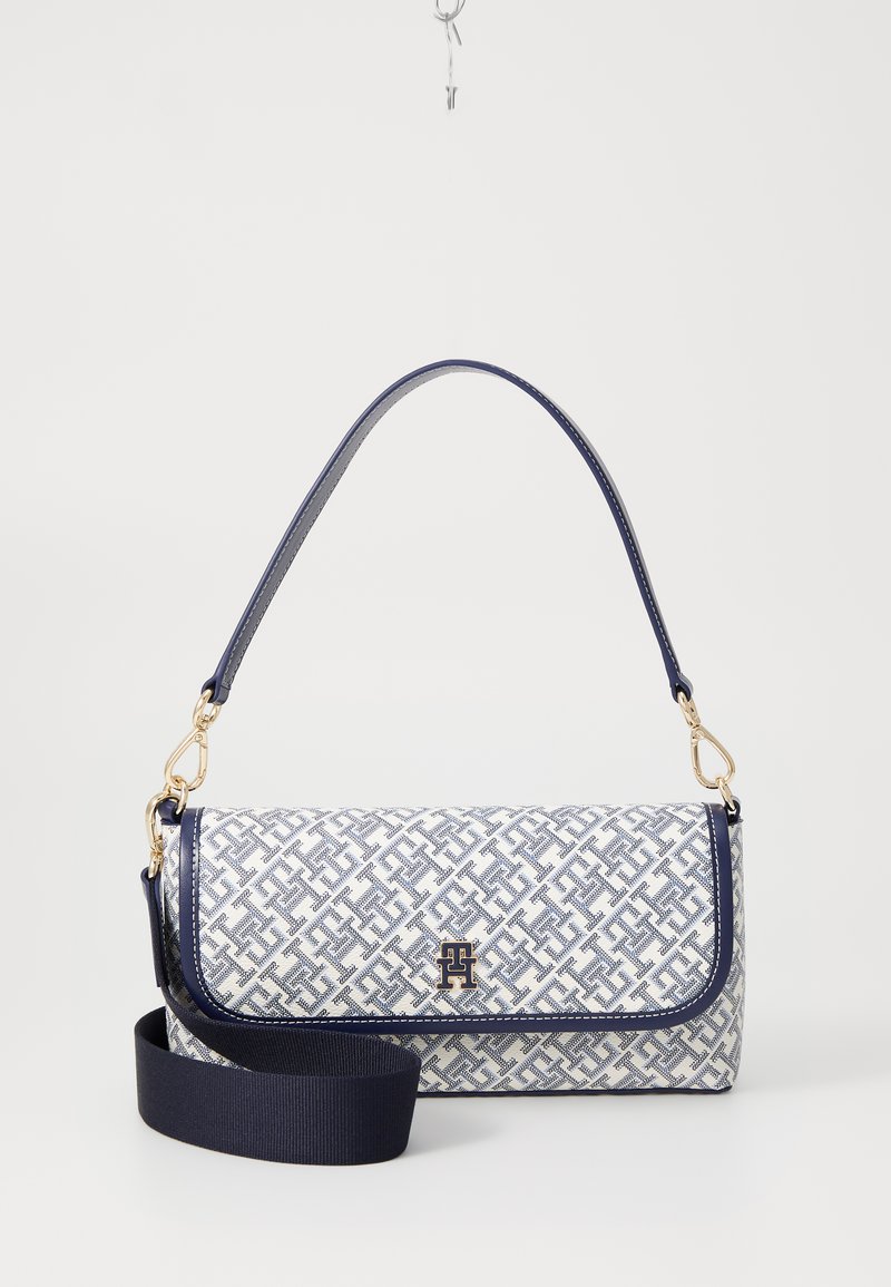 Bolsa texturizada com um padrão geométrico azul e branco, acabamento azul marinho, detalhes em metal dourado e uma alça de ombro removível.