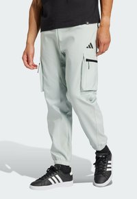 Lichtgroene joggers van gladde stof met elastische boorden, voorzien van ritssluitingen in de zijzakken en Adidas-logo-accenten.