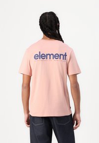 Lyserød bomulds t-shirt med et stort marineblåt logo på bagsiden. Designet inkluderer korte ærmer og en rund halsudskæring.
