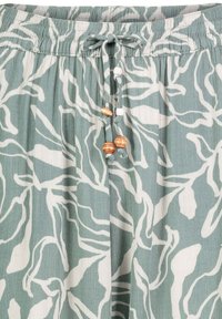 Lightweight, green blouse with white abstract floral patterns. Features a gathered waistband and a drawstring with decorative beads.