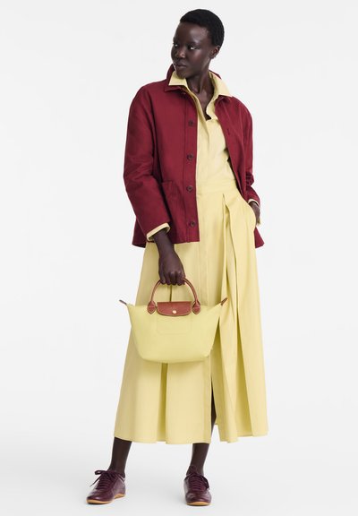 Rote Baumwolljacke über einem gelben Kleid mit Falten, kombiniert mit einer gelben Handtasche mit braunen Akzenten und burgunderroten Sneakers.