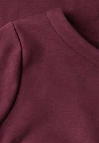 Tessuto di cotone bordeaux, dalla consistenza liscia, con scollo a giro e maniche corte, che enfatizza un design semplice e casual.