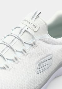 Scarpa sportiva bianca con tomaia in rete testurizzata, lacci elasticizzati e suola grigia chiara. Presenta il logo Skechers sul lato.