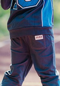 Mörkblå joggingbyxor med orange sömmar, med sidofickor och en vit "18AG" etikett. Mjuk och ledig passform.