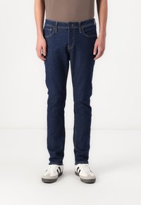 Jeanși de denim de culoare albastră închisă pentru bărbați, cu croi slim, având cinci buzunare, cusături galbene contrastante și o închidere clasică cu buton.