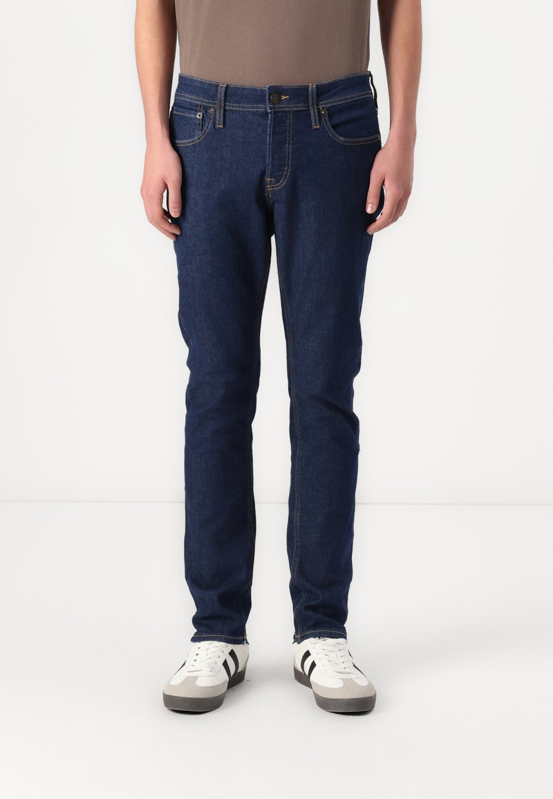Jeanși de denim de culoare albastră închisă pentru bărbați, cu croi slim, având cinci buzunare, cusături galbene contrastante și o închidere clasică cu buton.