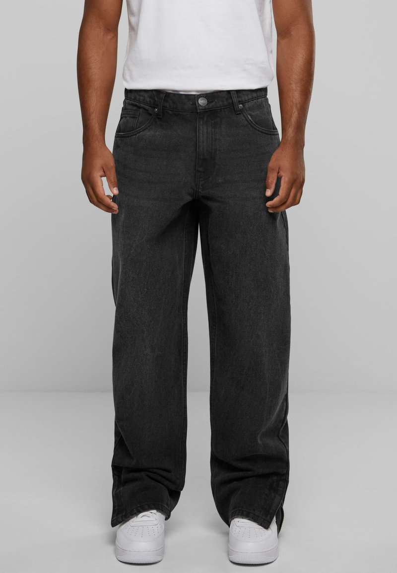 Black straight-leg jeans made of denim, featuring five pockets, a button closure, and a faded texture. Worn with white sneakers.