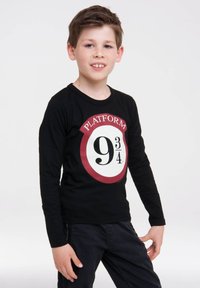 Schwarzes langärmliges T-Shirt mit einem kreisförmigen roten und weißen Grafik, das "PLATFORM 9¾" und eine große schwarze Ziffer "9" auf der Vorderseite zeigt.