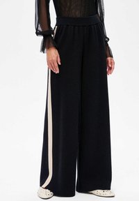 Zwarte wijde broek van zachte stof, met een contrasterende crèmekleurige verticale streep, elastische tailleband en een ontspannen pasvorm.