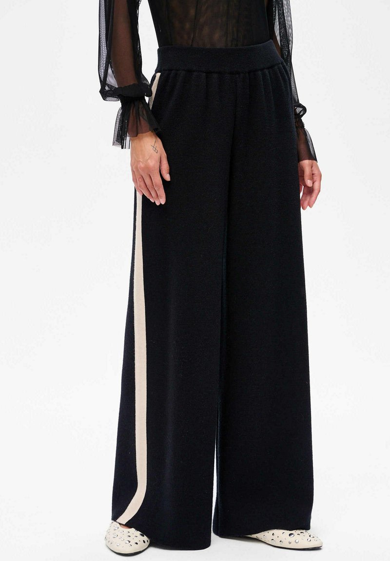 Zwarte wijde broek van zachte stof, met een contrasterende crèmekleurige verticale streep, elastische tailleband en een ontspannen pasvorm.