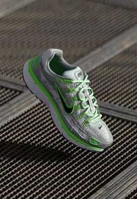 Sive tenisice s zelenim detaljima, mrežasti gornji dio, teksturirana podloga i crni Nike swoosh logo, s podstavljenim okovratnikom i vezicama.