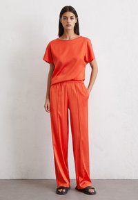 Red satin top with short sleeves and matching elastic-waist pants. Loose fit, smooth texture, paired with black sandals.