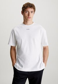 White cotton t-shirt with a crew neckline, short sleeves, and a small black "Calvin Klein" logo on the chest. Smooth texture.