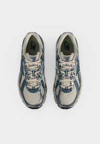 Двойка бели и сини маратонки New Balance с мрежеста материя и връзки, гледани отгоре на чист фон.