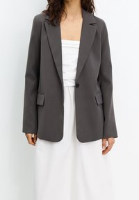 Blazer gris avec revers en pointe, fermeture à un bouton et deux poches avant. Tissu lisse, coupe cintrée et manches longues.