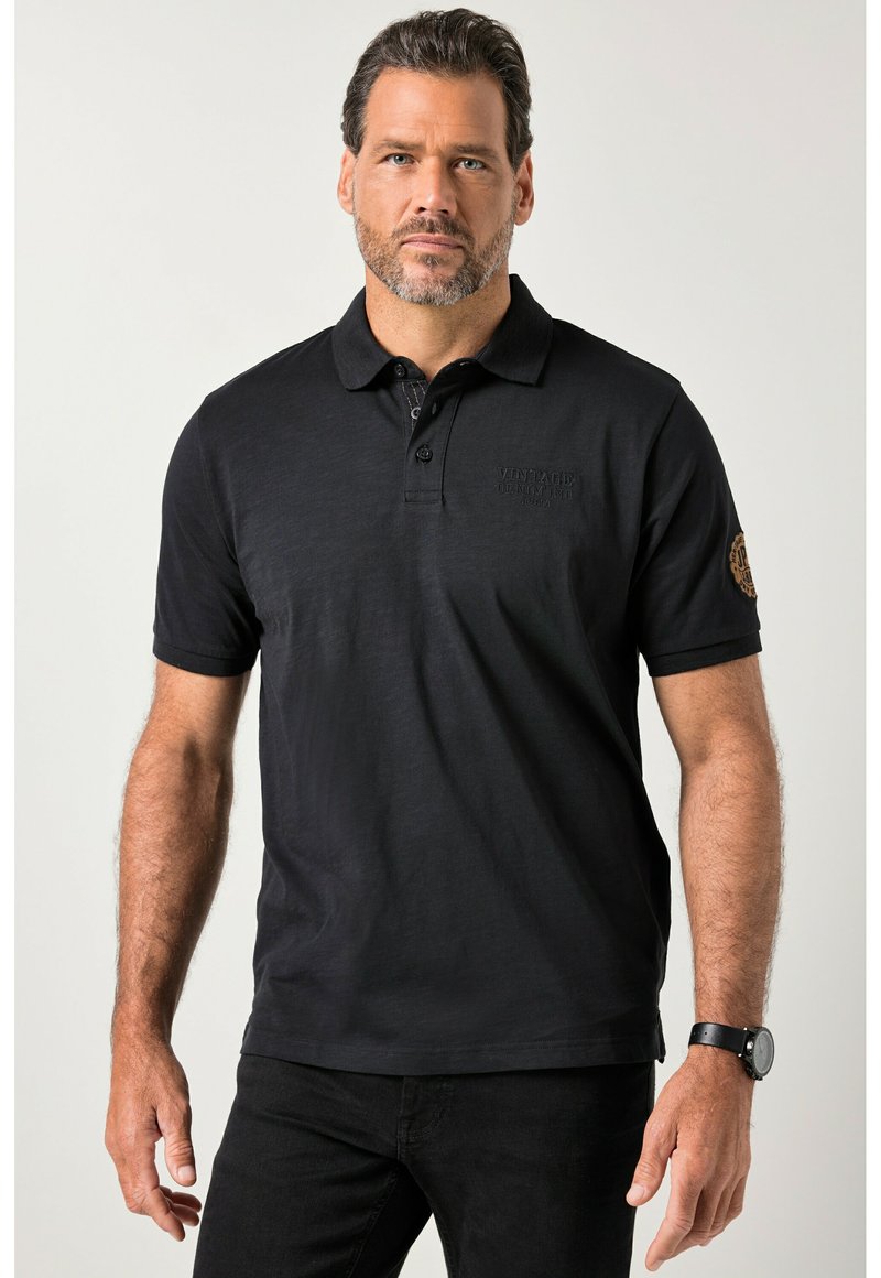 Musta pehmeästä kankaasta valmistettu poolopaita, jossa on kolmen napin läpyskä, kirjailtu logo ja koristeellinen merkki hihassa.