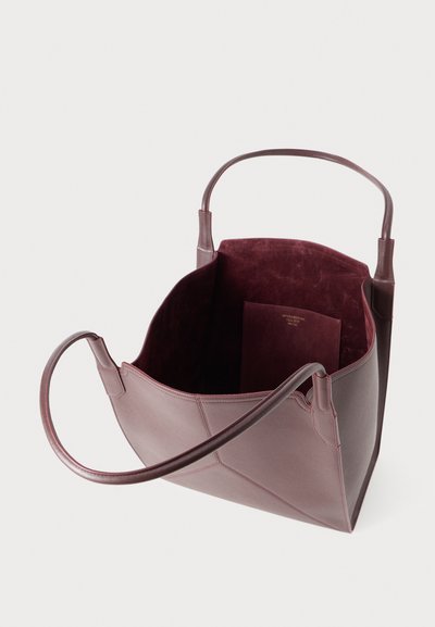 Open deep burgundy leather tote bag with two round handles and a suede interior pocket against a white background.