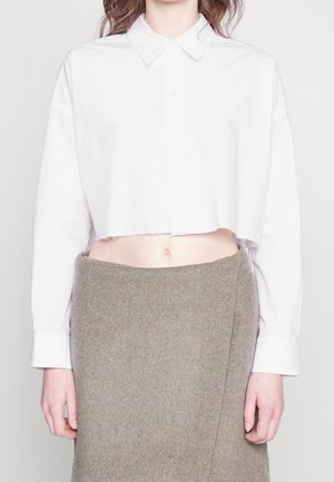 Gekürztes weißes Langarmhemd mit rohem Saum kombiniert mit einem hoch taillierten grauen Wollrock, das den bloßen Bauch zeigt.