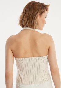 Helle beige trägerlose Bluse mit vertikalen schwarzen Streifen, körpernahe Passform und glatter Textur. Rückansicht zeigt minimale Bedeckung und maßgeschneiderte Passform.