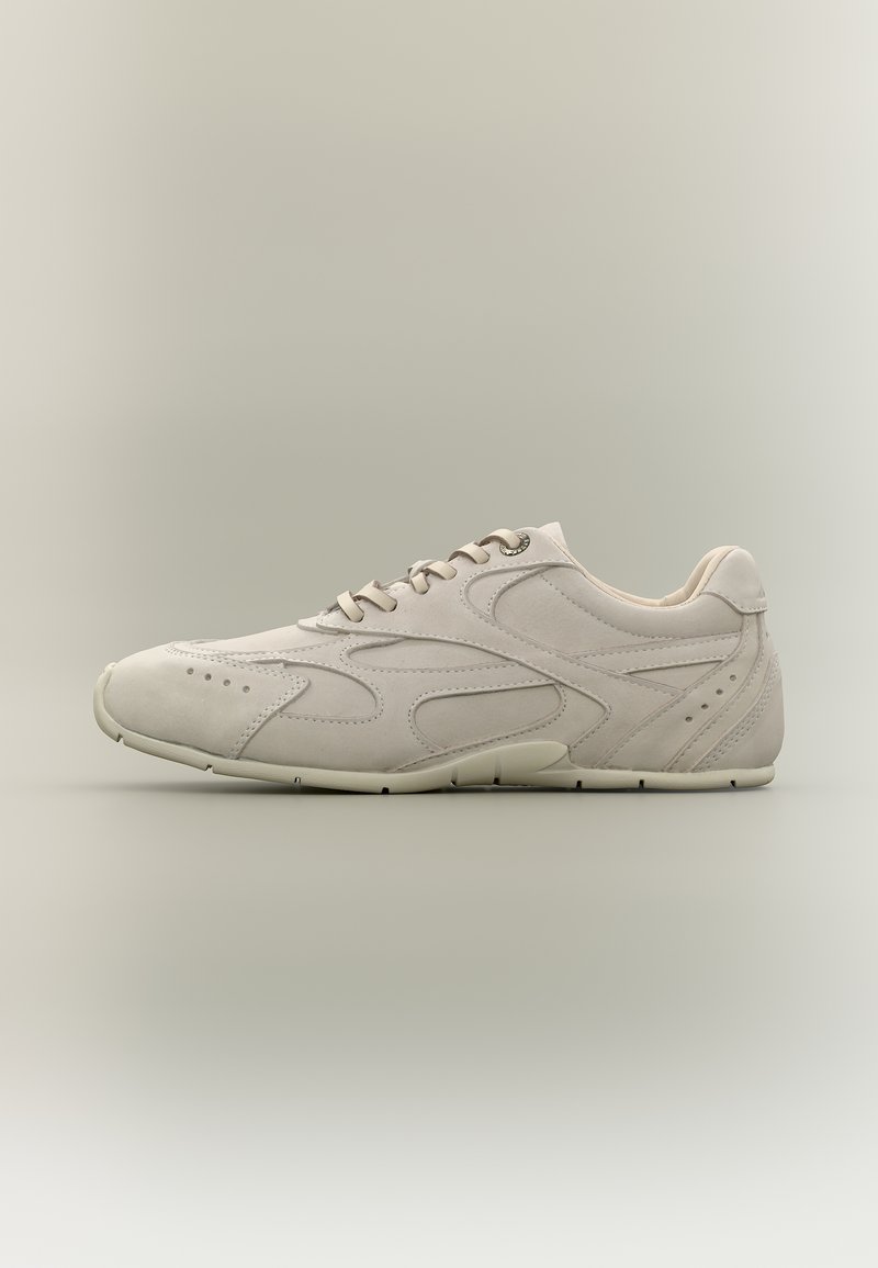 Biały niski sneaker z przodu na sznurowadła, z przeszyciami tworzącymi wzory faliste oraz perforacjami na obszarach palców i pięty, widziany z boku.