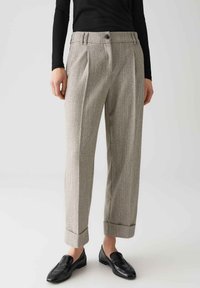 Pantaloni su misura grigi, texture con due pieghe frontali, tasche laterali e risvolti. Abbinati a mocassini neri e a un top nero a coste.