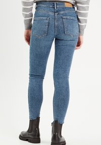 Tight-fit blå jeans med en tekstureret denim finish, der har to baglommer, en høj talje og en lynlåsdetalje ved anklen.