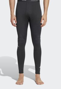 Sorte atletiske tights har et tætsiddende design, blød tekstur og ribbede detaljer langs benene, med et logo på waistbandet.