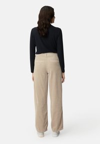 Black long-sleeve top, beige wide-leg corduroy pants with textured surface, back pockets, and white sneakers on a neutral background.